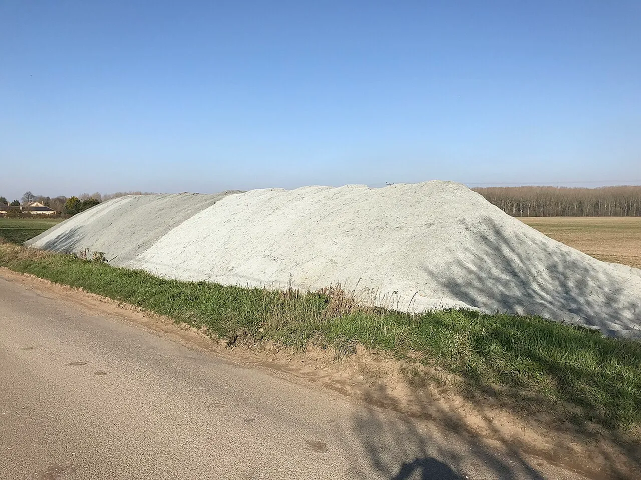 A large heap of pale agricultural lime at the edge of a farm field.