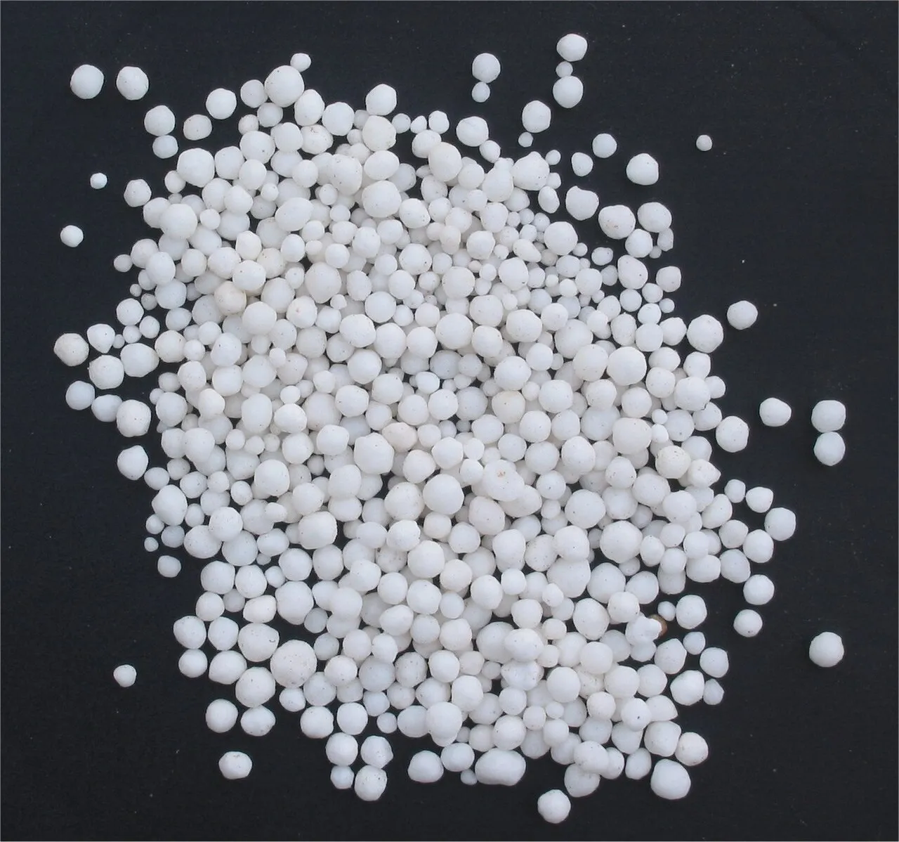 White nitrogen fertilizer prills spread on a black surface.