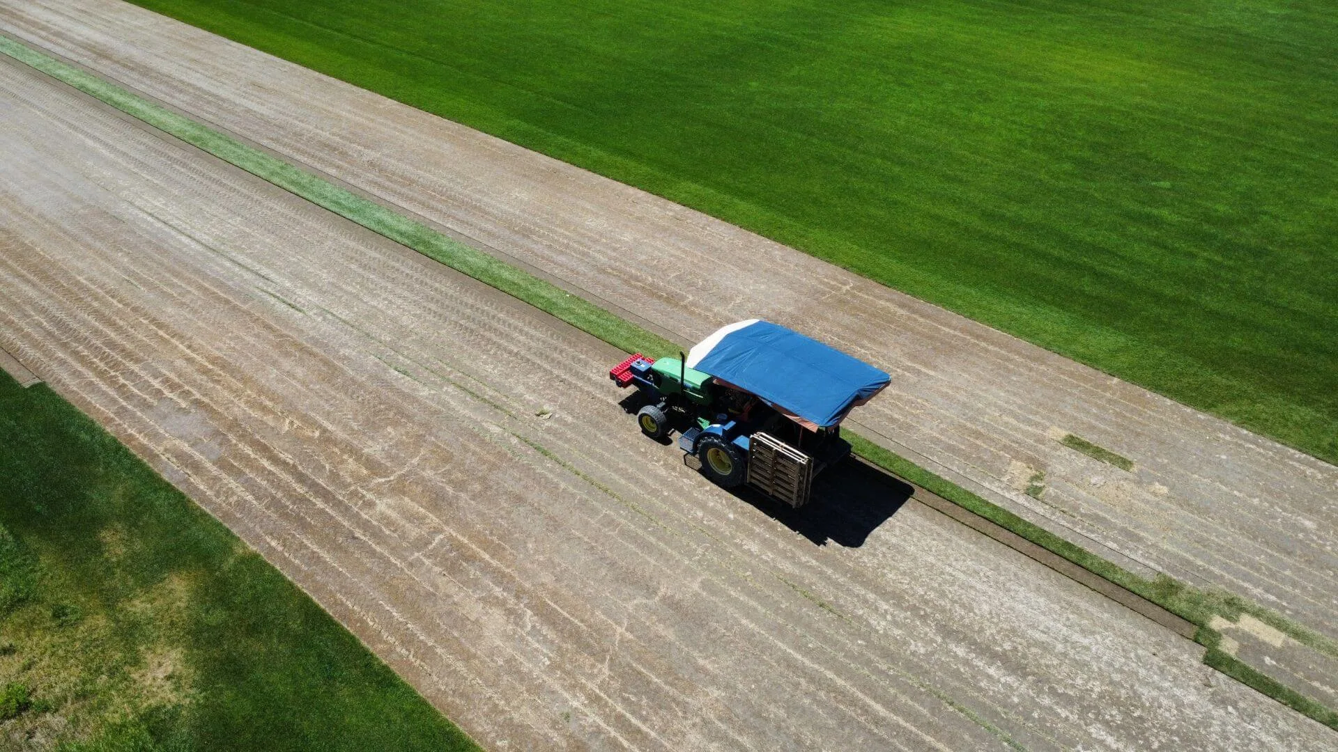 Aerial view of a sod harvester cutting a strip of turf, with bare harvested ground on one side and deep green field on the other.