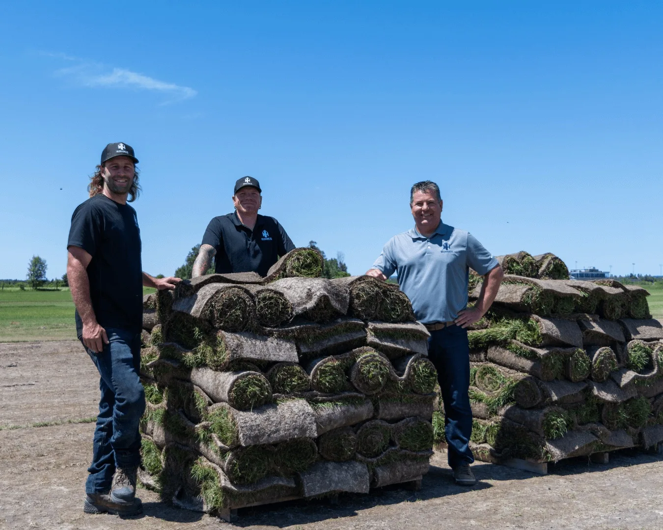 Three members of the North Range Sod team standing beside pallets of freshly harvested sod rolls in the field.