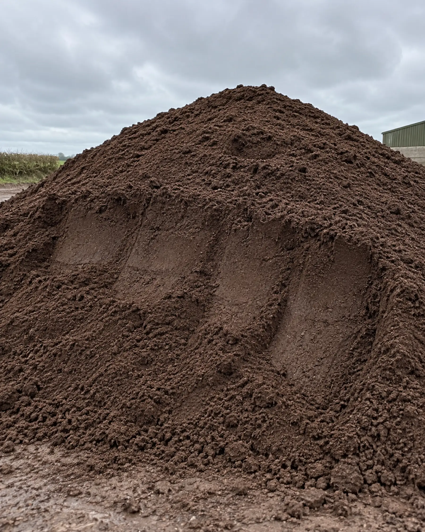 A screened pile of dark, fine-textured loam top soil on a farm yard.